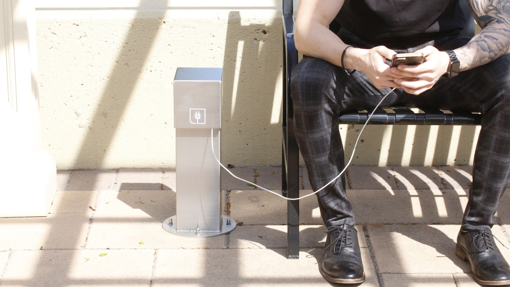 A man sitting on a bench charging his phone with a power pedestal
